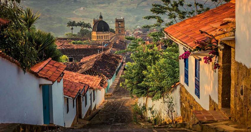 Fotografía de calle de Barichara, con casas antiguas a los lados y al fondo la iglesia y su cúpula.