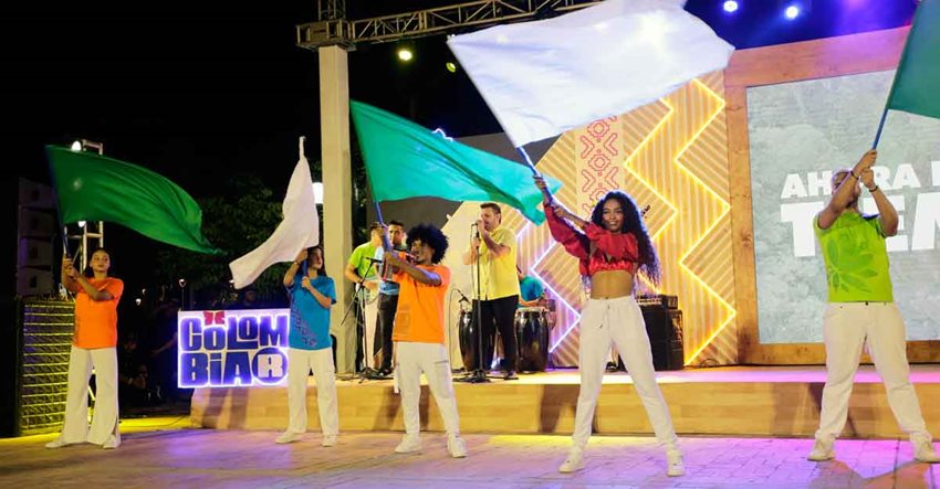 Jóvenes con camisetas de colores moviendo banderas blancas desde un escenario.