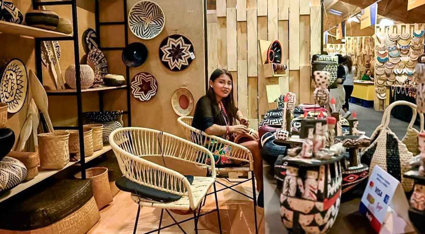 Mujer artesana sentada en su estand, junto a las artesanías que vende.
