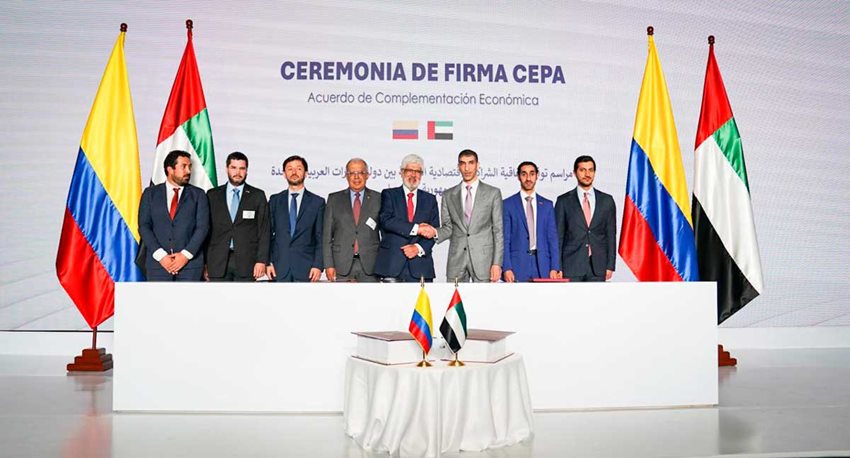 Ocho hombres, funcionarios de Emiratos Árabes Unidos y Colombia, en el escenario, al lado de banderas.