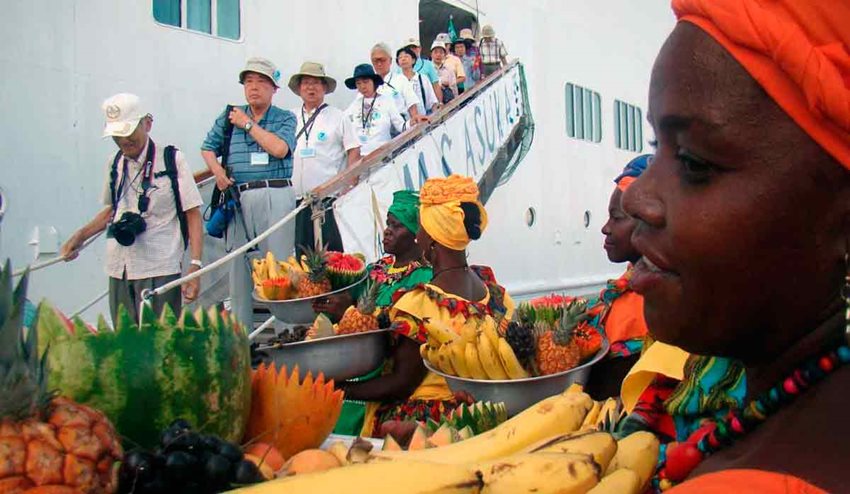 Personas bajando de un barco y caminando hacia mujeres de color con trajes típicos de la costa colombiana.