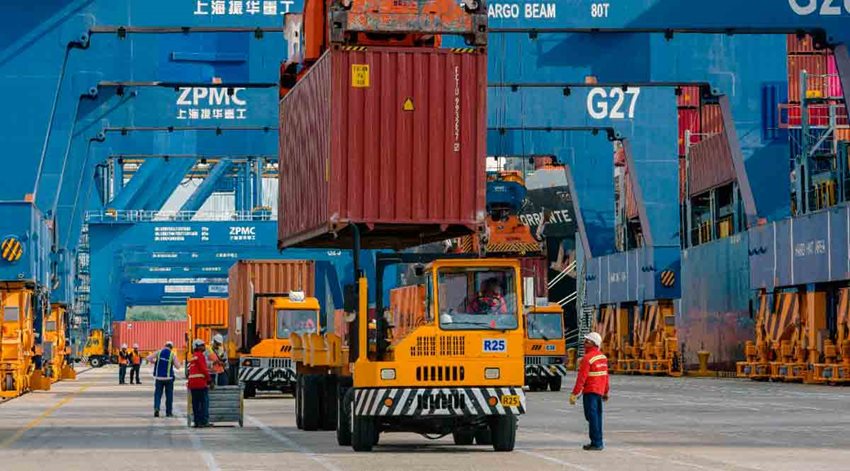 Camiones amarillos transitando con contenedores rojos por vías de zona franca.