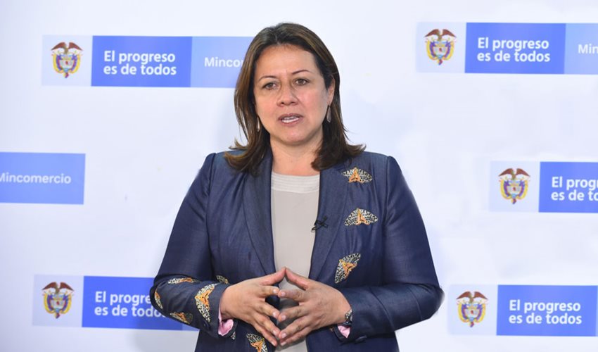 Ministra Ximena Lombana, con traje azul, dando declaraciones, con un fondo con el logo de Mincomercio.