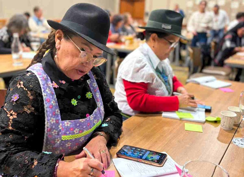 Mujeres vestidas de campesinas, escribiendo sobre papeles puestos en mesa.