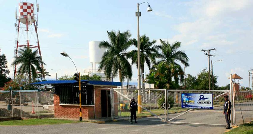 Fotografía de portería de un lote, con dos celadores, palmas y un tanque de agua al lado.