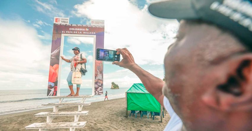 Hombre tomando foto a mujer posando en escaleras, en la playa, con letrero de 