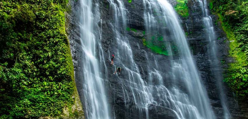 Panorámica de caída de cascada, con personas descendiéndola.