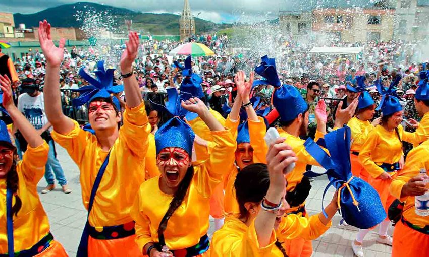 Personas vestidas de amarillo y naranja, con gorros azules, celebrando en medio de unas fiestas en Pasto.