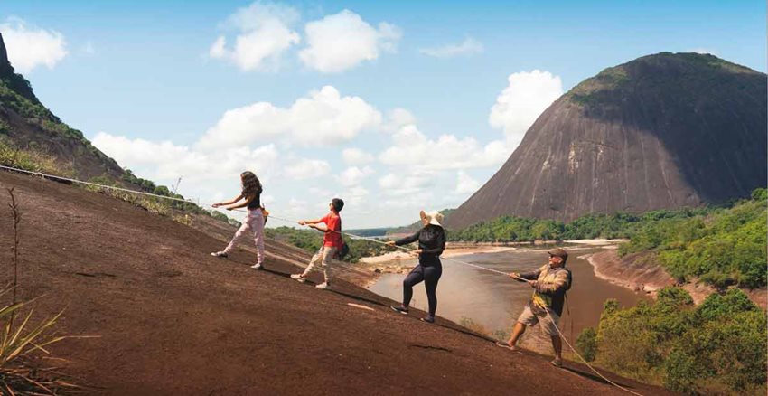 Tres mujeres y un hombres subiendo una montaña agarrados de una cuerda.