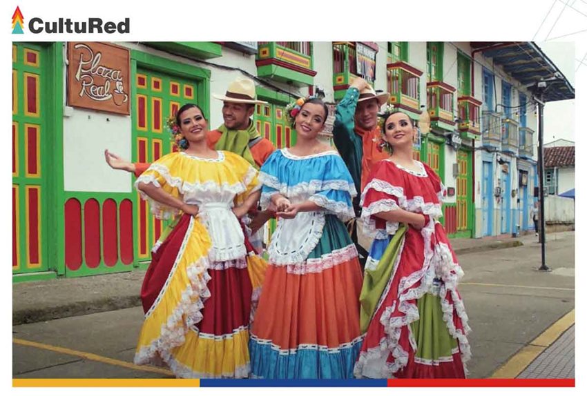 Dos hombres y tres mujeres, con trajes típicos de Colombia, posando en medio de la calle de un pueblo.