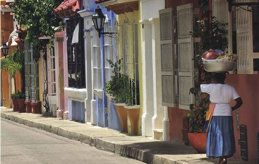 Palenquera caminando por las calles del centro histórico de Cartagena, frente a casas de colores.