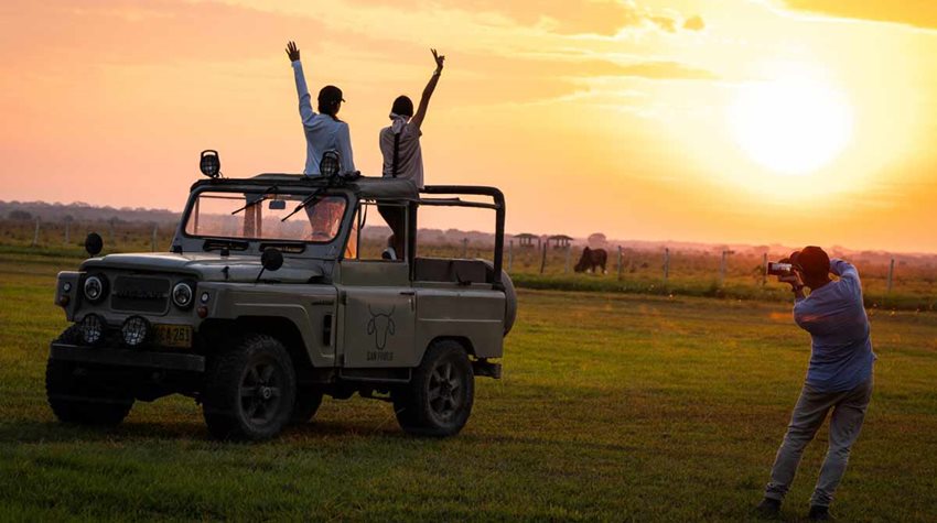 Hombre tomándole una fotografía a unas chicas en un Jeep mientras observan el atardecer.