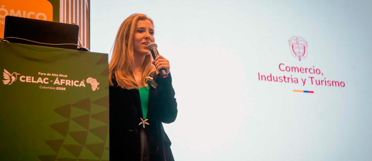 Descripción imagen: Sofía Cañón hablando por micrófono desde el escenario, con el logo del MinCIT al fondo.