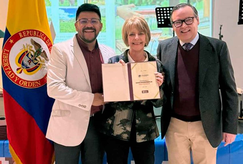 Dos hombres y una mujer, sosteniendo un diploma en sus manos, posando para la foto con la bandera de Colombia.