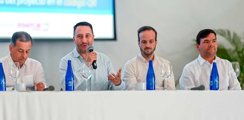Cuatro hombres con camisas blancas, sentados frente a una mesa hablando al público.