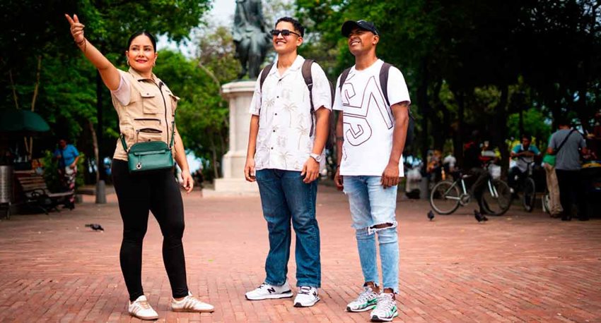 Una mujer, guía turística, mostrando el parque de un pueblo a dos hombres.