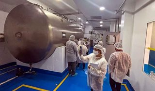 Personas con elementos y trajes de seguridad caminando por pasillos de planta de manufactura.