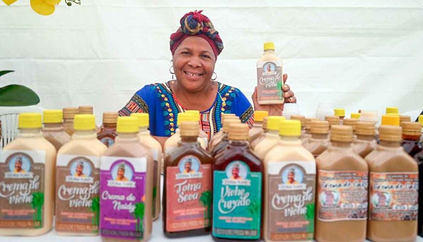 Mujer morena, vestida con ropa autóctona de la región pacífica, exponiendo sus productos en botellas.