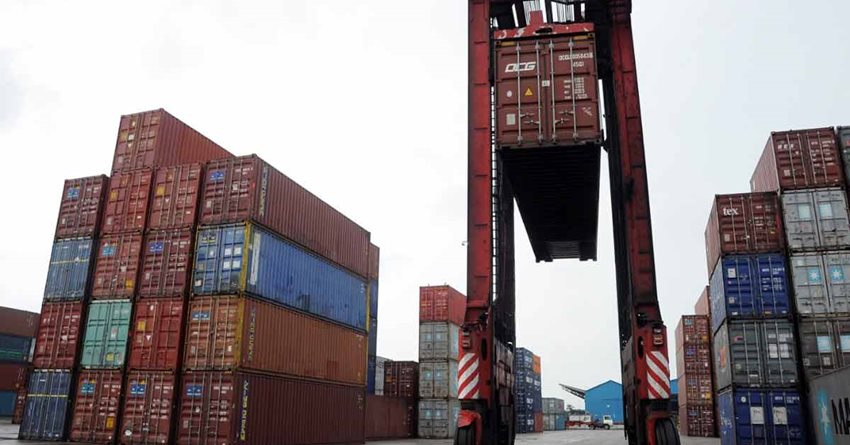 Calle de zona franca con contenedores de colores descargados y máquina de carga parqueada.