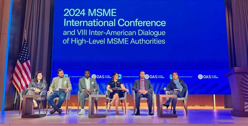 Tres hombres y tres mujeres sentadas en sillas en el escenario, dando una charla.