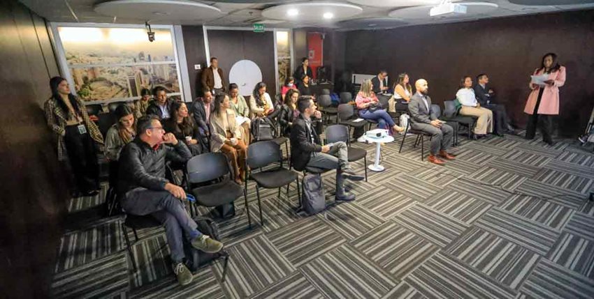 Hombres y mujeres sentados prestando atención al frente a quien habla.