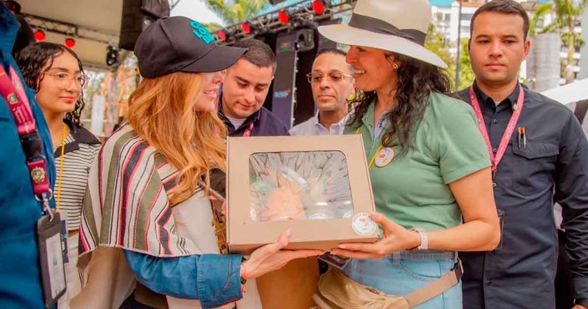Ministra Diana Marcela Morales recibiendo un detalle de una mujer, en medio de personas que las rodean.