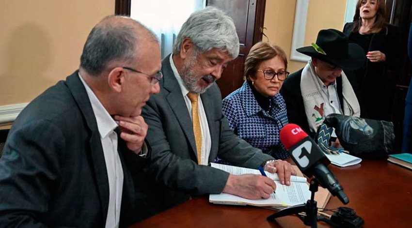 Ministro Germán Umaña, rodeado de funcionarios del Gobierno, firmando un documento.