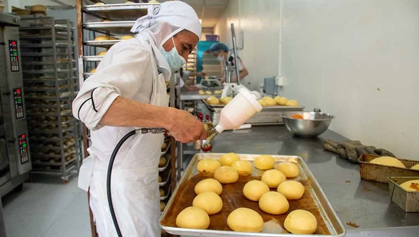 Hombre con traje blanco de higiene, trabajando en cocina de panadería.