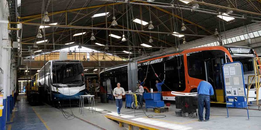 Hombres arreglando dos buses eléctricos en un taller.