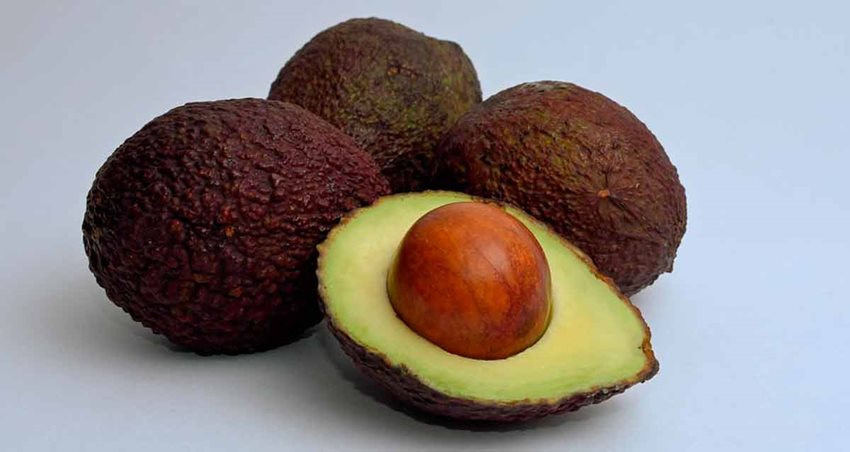 Fotografía de tres aguacates Hass enteros y una a la mitad, con la pepa visible.