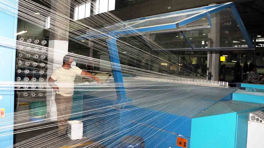 Hombre de pie frente a máquina de hilar mientras ésta está en funcionamiento.