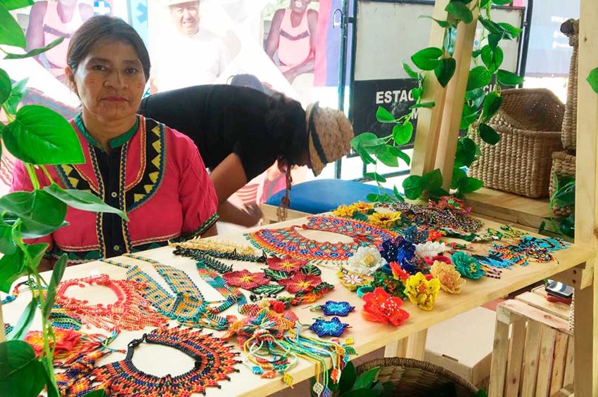 Mujer indígena con traje rosado exponiendo sus artesanía y accesorios fabricados a mano.