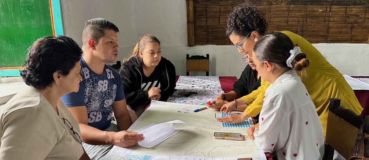 Descripción imagen: Personas reunidas alrededor de una mesa rectangular, mirando documentos en medio de una conversación
