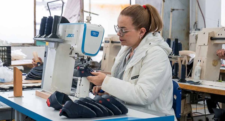 Mujer con chaqueta blanca, gafas y cabello recogido trabajando en máquina de coser.