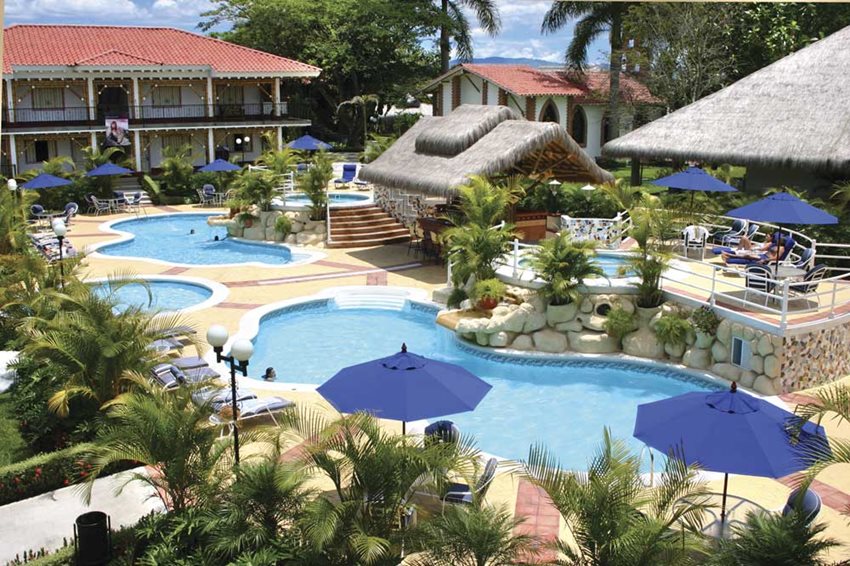Zona de piscinas en un hotel, con cabañas y palmeras.