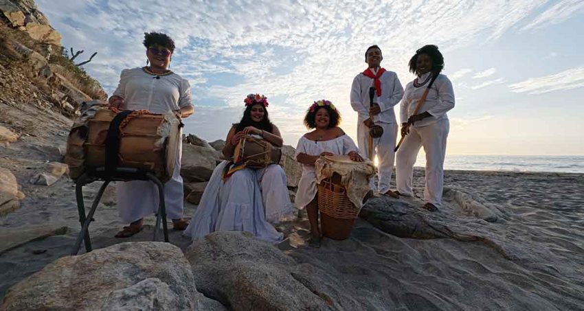 Hombres y mujeres, de blanco, con instrumentos típicos colombianos, en una playa.