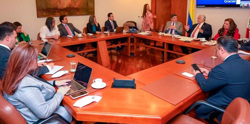 Hombres y mujeres reunidos alrededor de mesa cuadrada, dialogando.q