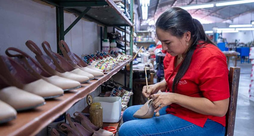 Mujer, con camisa roja y cabello recogido, sentada pegando tacones de color beige.