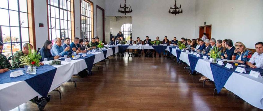 Hombres y mujeres reunidos alrededor de mesa cuadrada, dialogando.