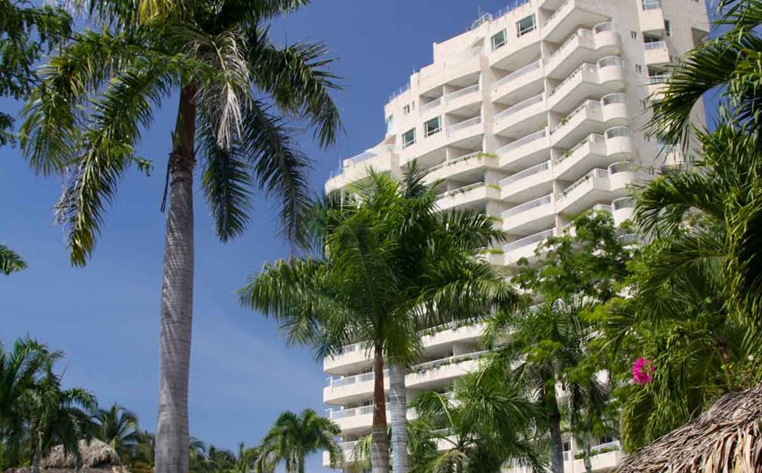 Foto de edificio blanco con palmeras alrededor.