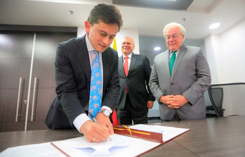 Tres hombres en traje de corbata firmando documento sobre una mesa.