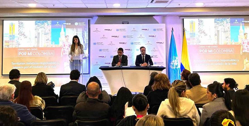 Presentadora, dos hombres expositores y el público prestando atención.