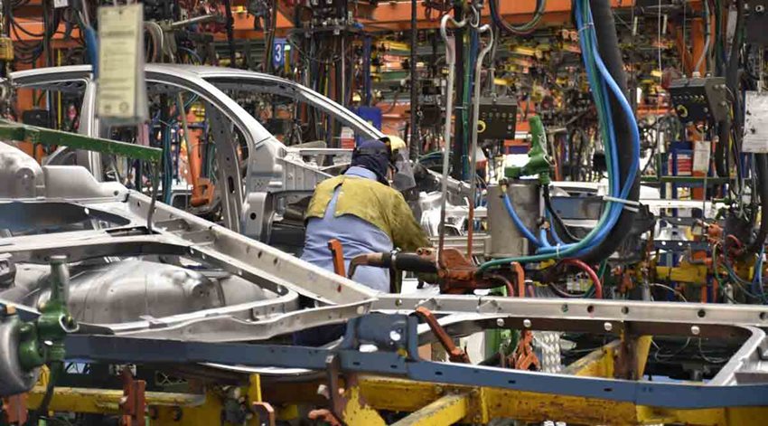 Hombre, con traje de seguridad, trabajando en medio de una fábrica que ensambla carros.