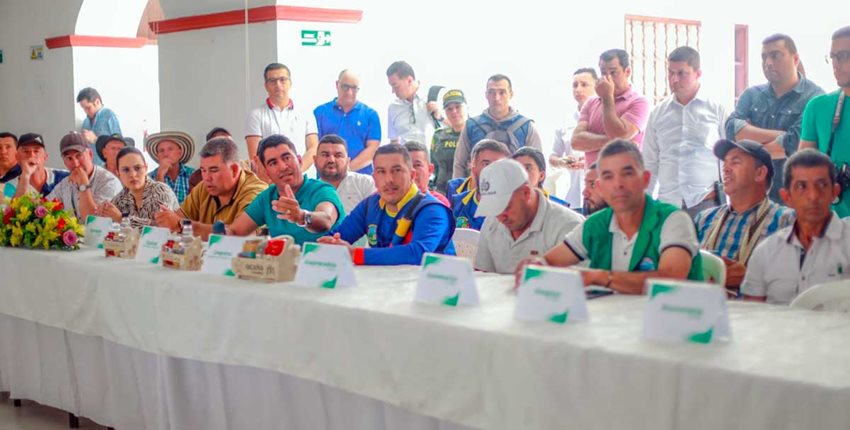 Personas sentadas en mesa rectangular, hablando en medio de una reunión.