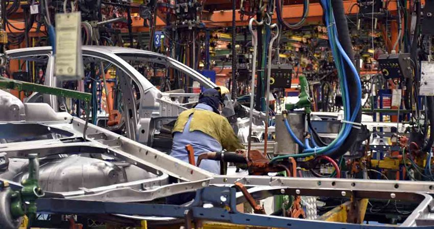 Hombre, con traje de seguridad, trabajando en medio de una fábrica que ensambla carros.