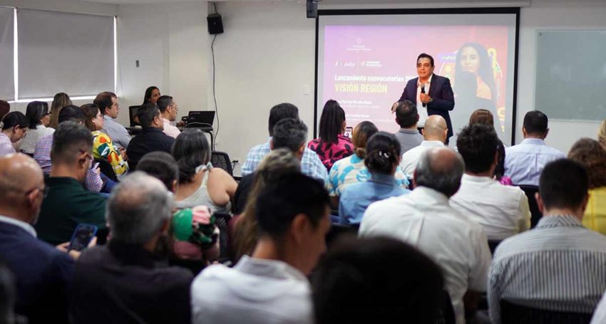 Hombre en frente, hablando por micrófono al público asistente.