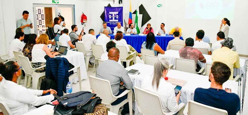 Personas sentadas en sillas, dentro de un auditorio, prestando atención a los ponentes.