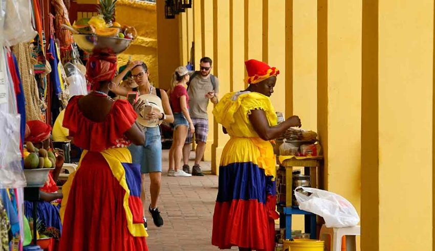 Turistas caminando por mercado de Cartagena, en medio de palenqueras.