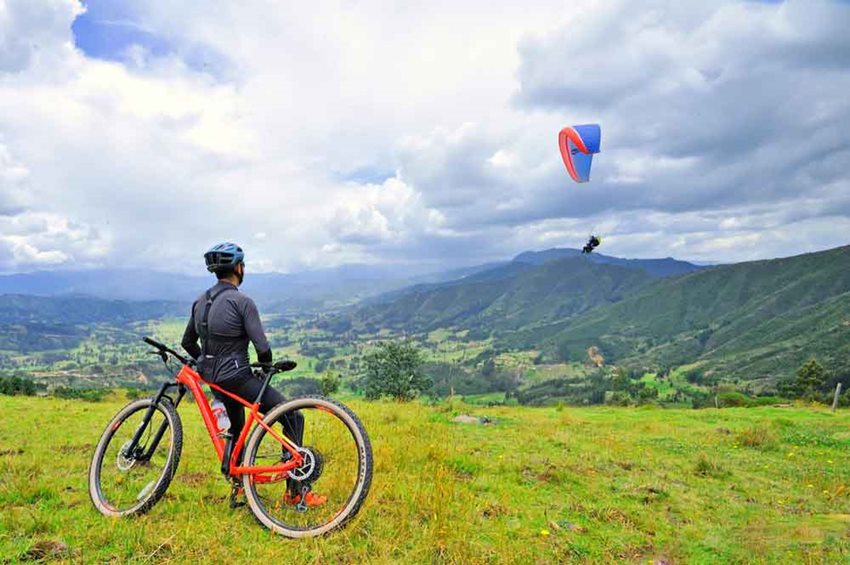 Ciclista en una montaña viendo cómo hacen parapente.