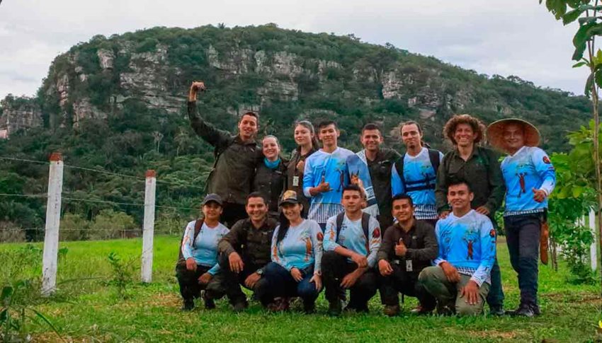 Hombres y mujeres posando para la foto, en medio del campo, con montañas de fondo.